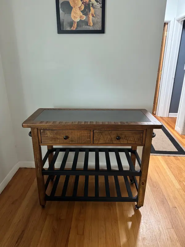 Rustic kitchen island cart or entry table in solid wood with a black iron base and lower storage shelf. Inset stone-look top, two deep drawers with iron pulls, and locking casters so it rolls where you need it and stays put when you're working.

Dimensions:  42" W  x 18" D  x 34" H 

Roughly [W x D x H] — the right size for a small kitchen that needs prep space, or as a bar cart / coffee station. Excellent condition, no wobble, drawers slide clean. Comparable pieces run $400–600 new.

Moving out of state, so it's priced to go. Local pickup in South Burlington — fits in most SUVs with the seats down.