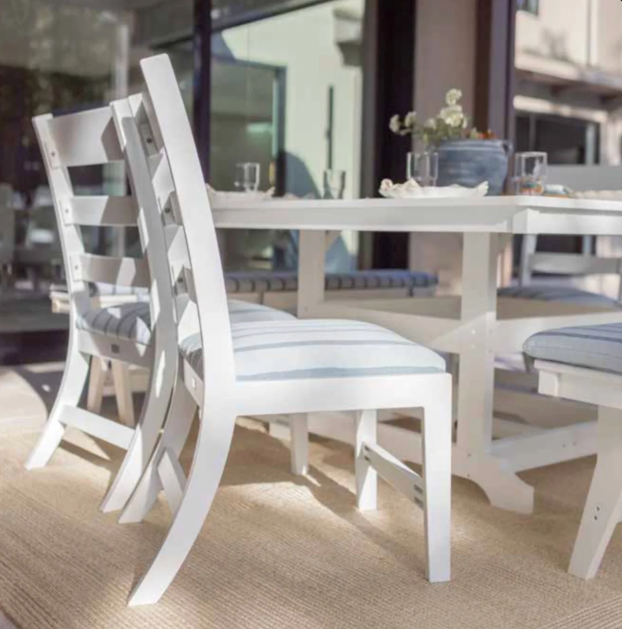 White slat-back outdoor dining chairs pulled up to a matching table with blue striped seat cushions