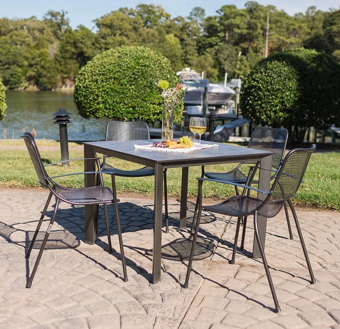 Kettler wrought iron patio dining set with four mesh-back chairs and a square table set for lunch beside the water