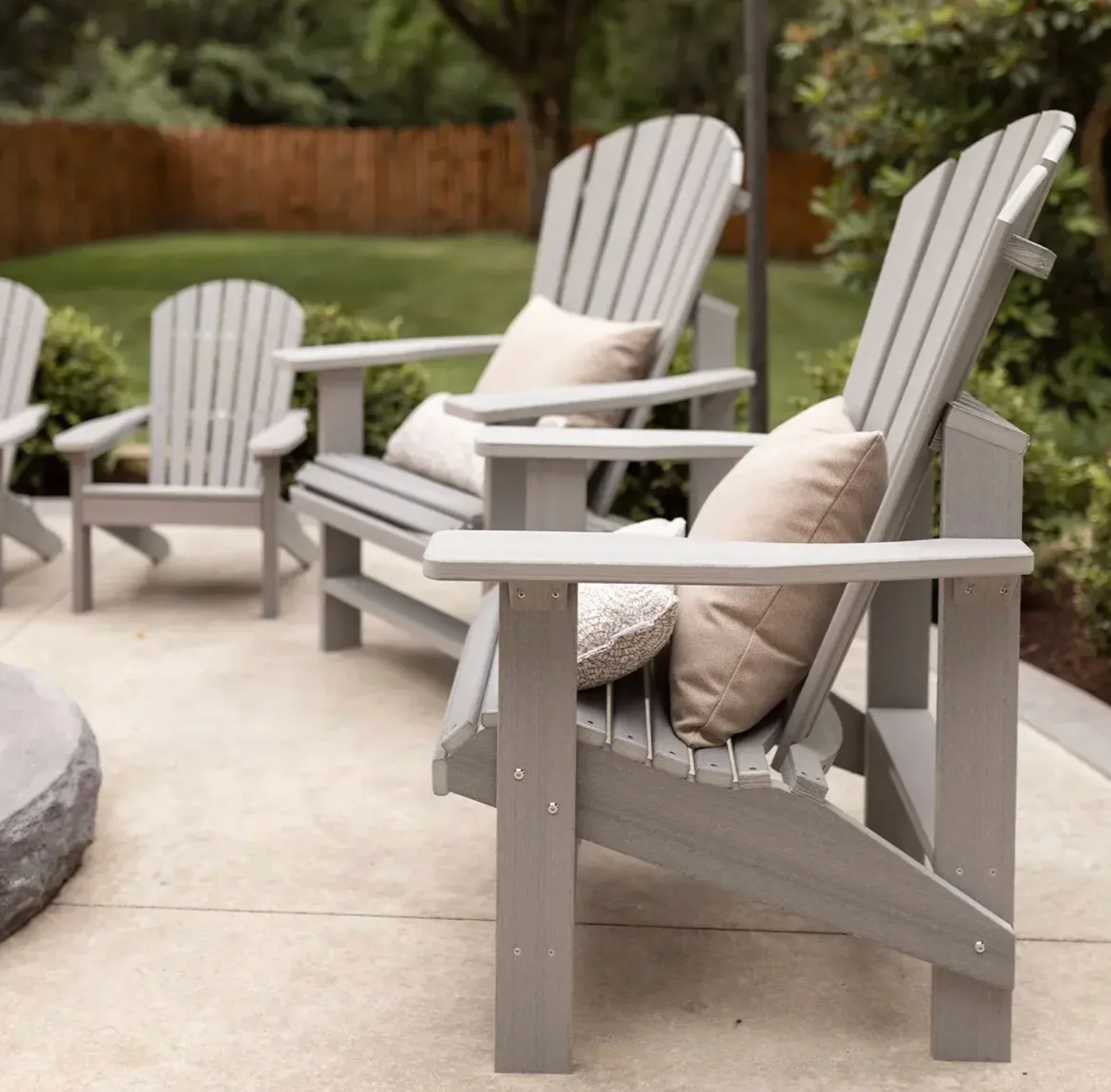 Grey poly Adirondack chairs with throw pillows grouped on a patio beside a garden