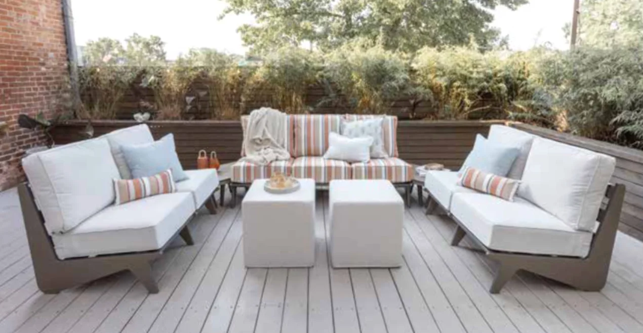 Outdoor deep-seating sofa and lounge chairs with white cushions and striped pillows arranged around a low table on a deck