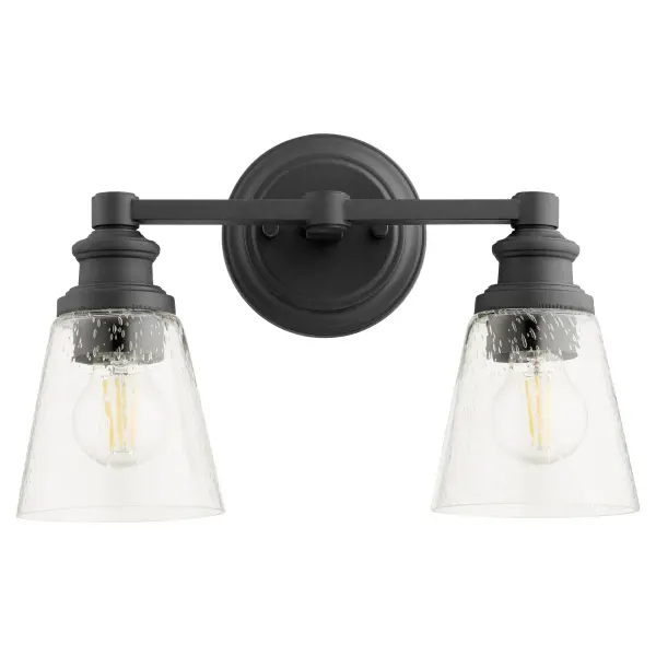 The Dunbar 2-Light Vanity blends nostalgic refinement with contemporary design through clear seeded glass shades and sharp angles. Features interchangeable socket cup decos in noir, satin nickel, and aged brass for personalization.