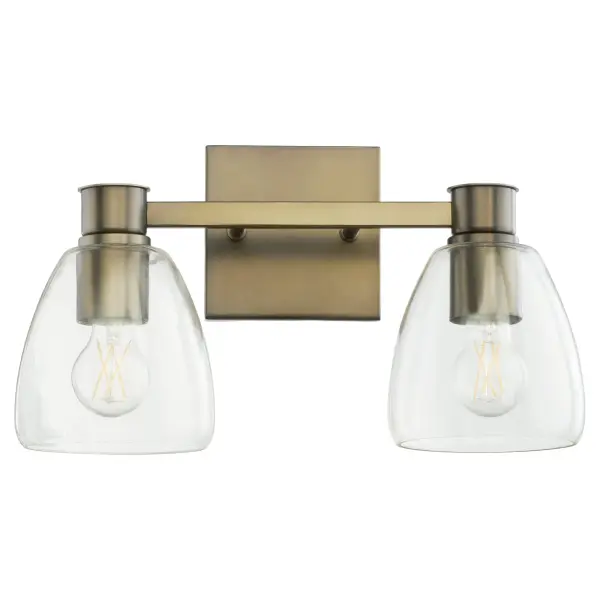 The Relo 2-Light Vanity combines traditional bell-shaped clear glass shades with a sophisticated dark brass frame, creating a transitional aesthetic that works in both classic and contemporary bathrooms.