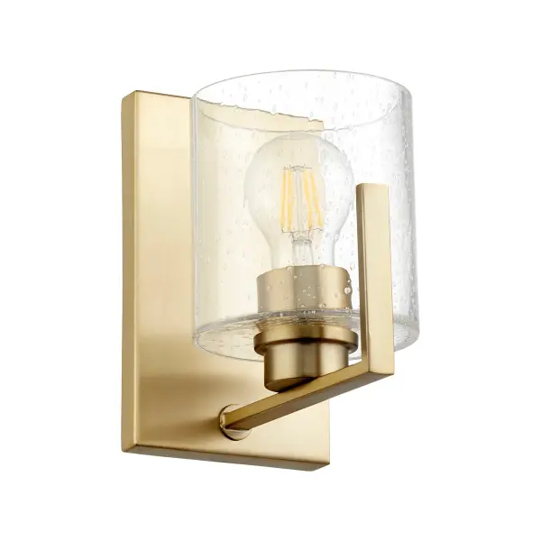This single-light wall sconce combines classic seeded glass with warm aged brass for a versatile fixture that works in traditional and transitional spaces. The rectangular backplate and round shade create visual interest.