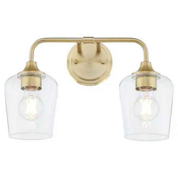 The Raymond 2-Light Vanity combines simple elegance with practical functionality. Featuring tapered clear glass shades and aged brass finish, this fixture delivers warm, ambient lighting perfect for bathrooms and powder rooms. - alternate view