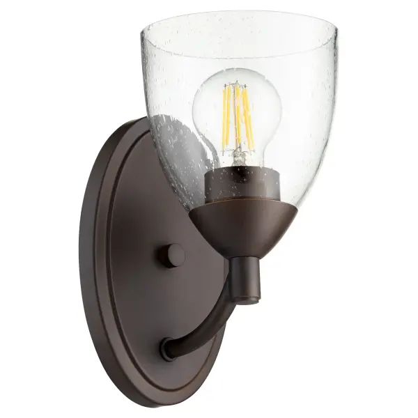 The Barkley wall sconce features sinuous tube frames and clear seeded glass that bridges traditional and contemporary styles. Its clean lines and oiled bronze finish offer timeless elegance for various interior settings.