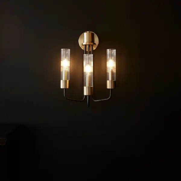 The Helix 3-Light Wall Sconce combines minimalist design with mid-century modern aesthetics. Its linear frame features soft angular curves, complemented by a sophisticated two-tone Aged Brass and Noir finish with clear fluted glass shades. - alternate view