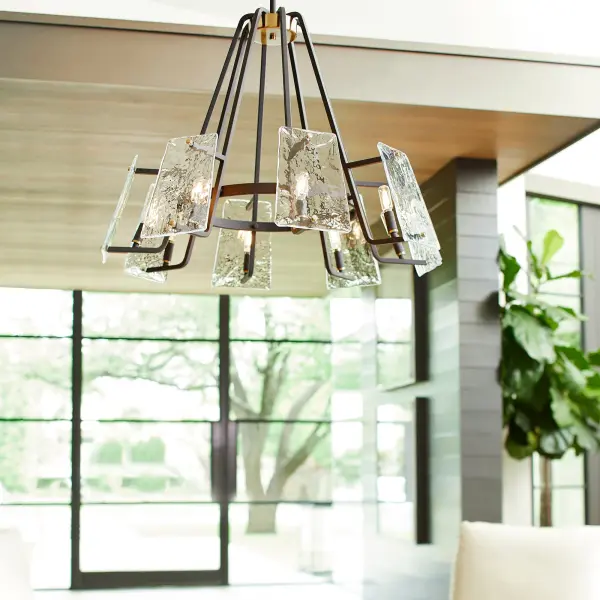 The Tioga 8-Light Chandelier combines nostalgic mid-century modern aesthetics with contemporary minimalist design. Featuring geometric framing, frosted glass trapezoid shades, and a striking noir finish with aged brass accents, this fixture creates a sophisticated focal point with free-floating illumination. - alternate view