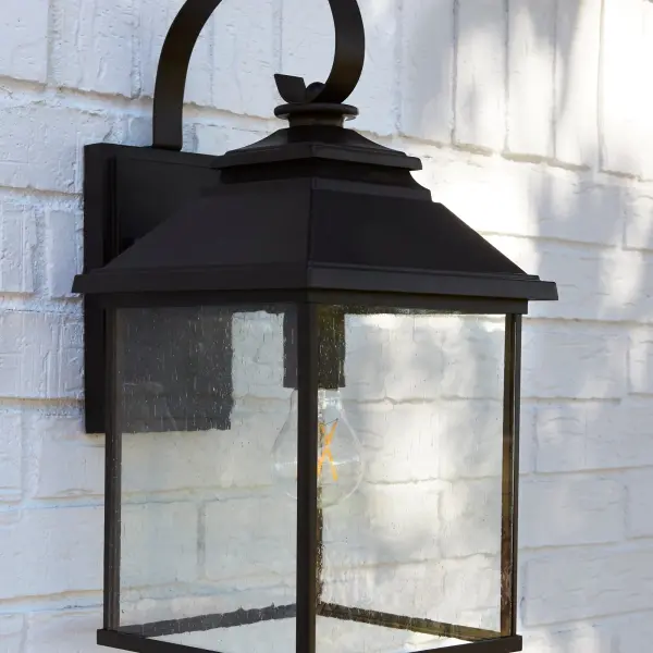 The Pearson outdoor wall lantern combines timeless traditional design with modern durability. Featuring an aluminum frame in a sophisticated black finish and clear seeded glass panels, this fixture delivers both style and function for outdoor spaces. - alternate view