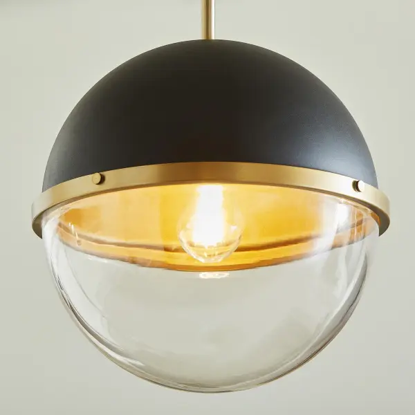 This eclectic pendant combines black and aged brass finishes with a distinctive dome-globe design. The vintage-inspired capture ring and decorative knobs add character, while the clear glass base provides ambient illumination. - alternate view