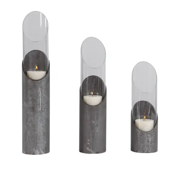 A set of three raw iron and clear glass candleholders in varying heights, styled with an angular, industrial silhouette and included beige candles for immediate use.