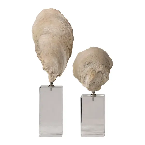 A charming set of two cast oyster shell sculptures in aged ivory with chrome accents, elevated on crystal cube bases for a polished tabletop display.