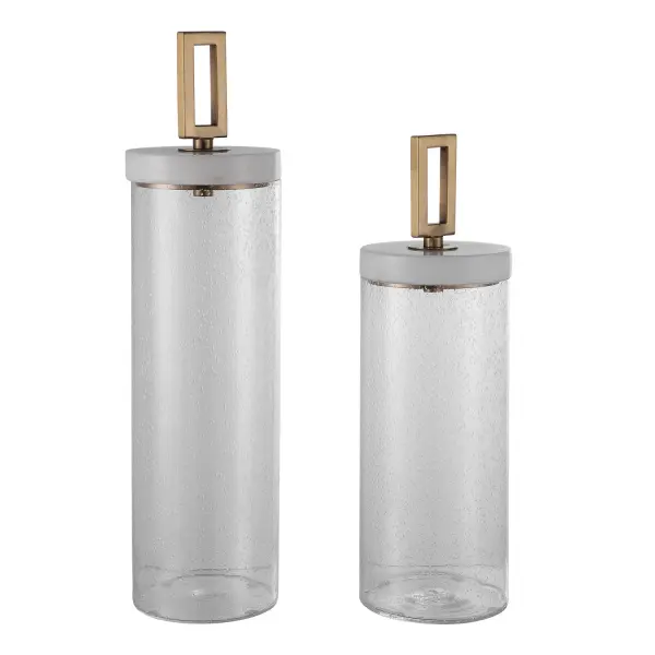 A set of two clear seeded-glass containers topped with white marble lids and brushed brass accents—decorative storage that doubles as a stylish accessory.