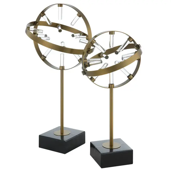 A set of two adjustable brass ring sculptures with crystal accents on black marble bases, offering an elegant, tactile decor moment for shelves or consoles.