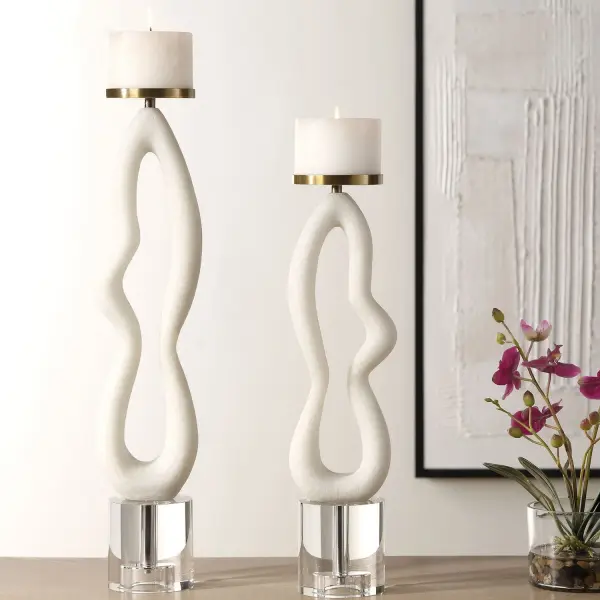 A set of two candleholders featuring an ivory man-made stone body resembling Thassos marble, accented with brushed brass iron details and crystal bases. Includes two white candles. Ideal for dining tables, consoles, or mantels indoors.