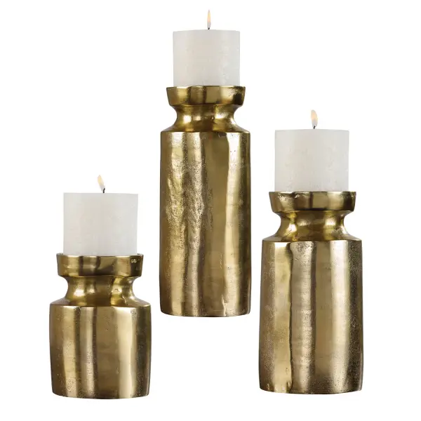 A set of three cast aluminum candleholders in an antiqued brass finish, each in a different height, with included white candles for instant styling.