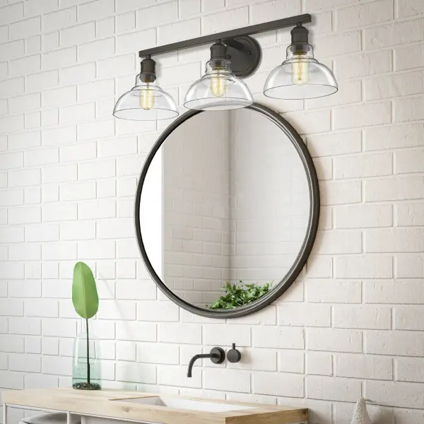 The Carver 3-Light Vanity combines timeless Rubbed Bronze finish with clear glass shades for brilliant, unobstructed illumination. Damp-rated for bathroom safety, this versatile fixture transitions seamlessly from farmhouse to industrial styles. - alternate view