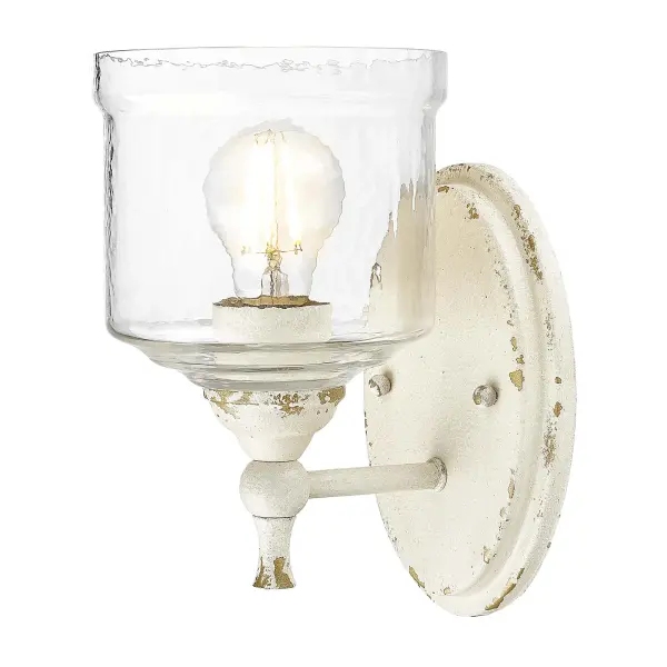 The Keating wall sconce combines vintage farmhouse charm with artisanal craftsmanship. Its antique ivory finish and hammered water glass shade create a warm, romantic ambiance perfect for traditional and shabby chic interiors.