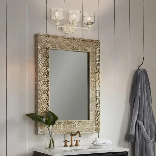 The Keating 3-light vanity combines traditional farmhouse charm with practical bathroom lighting. Its distressed Antique Ivory finish reveals hints of gold beneath, while hammered water glass shades create beautiful light refraction. - alternate view