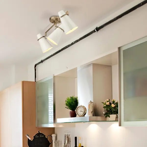The Reeva 3-light semi-flush mount combines mid-century modern aesthetics with practical adjustable directional heads. Its warm Modern Brass finish and creamy Glossy Ecru shades create an inviting ambiance while the damp rating extends placement options. - alternate view