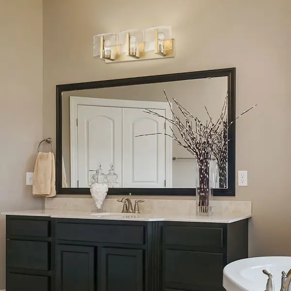 The Aenon 3-light vanity combines artisanal hammered water glass with brushed champagne brass for a sophisticated, nature-inspired aesthetic. Perfect for modern bathrooms seeking both practical illumination and decorative appeal. - alternate view