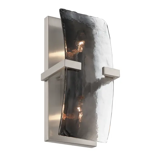 Aenon 2-light Wall Sconce offers a sophisticated balance of soft metal tones and textured glass. Finished in warm satin Pewter, the steel frame supports thick Smokey Water Glass panels inspired by natural ice and flowing water. The smoky gray glass tempers brightness while its hammered surface refracts light into layered highlights and shadows. With dimensions of 6.25"W x 13"H x 4.75"D, this damp-rated sconce is well suited for bathrooms, hallways, stairways, and refined accent lighting applications.
