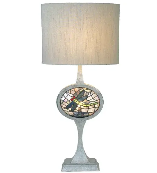 David Landis; renowned designer; has put his unique style on this lighted base stained glass lamp with fabric shade. The Silver hardback fabric shade tops a hand painted Nickel base that captures a jewel like oval dragonfly panel; with scarlet eyes; Pond Green tail and filigree wings.