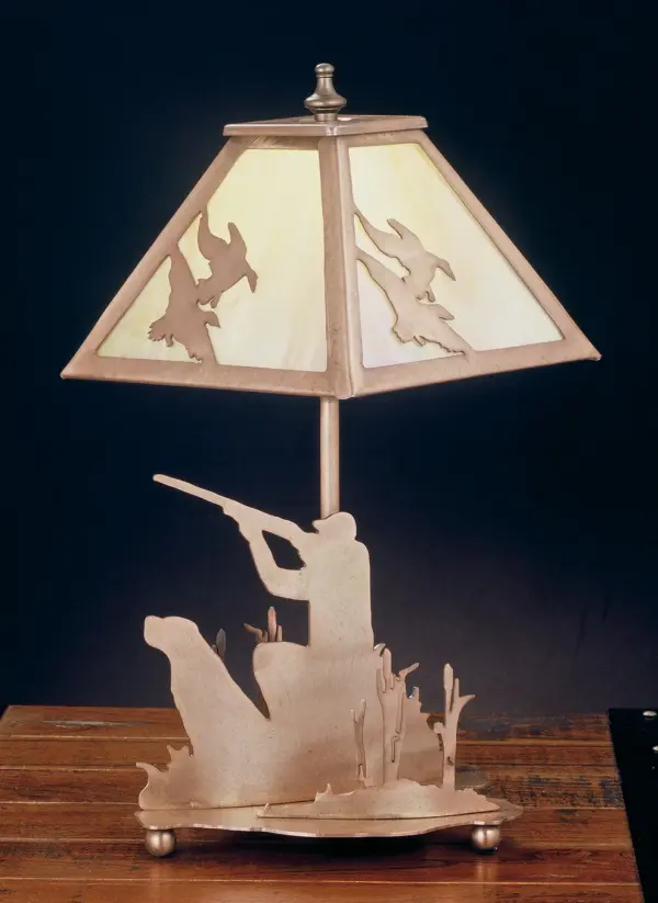 A linear square shade with ducks in flight sits above a lamp base that depicts a hunter and his retriever in a marshy blind. The accent lamp has an Antique Copper finish, has Amber mica panels and is handcrafted in the USA by Meyda artisans. Collection: Duck Hunter Finish: Antique Copper Antique Copper Glass: Amber Mica Width: 7.00" Height: 15.50" Length: 7.00" Number of Bulbs: 1 Maximum Wattage: 60.00 W Bulb Type: B10 Bulb Base: E12 Material: Steel Country of Origin: USA Safety Listing: Dry Safety Rating: Dry