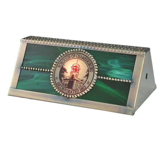 Perfect for crowning a banker's lamp base; this shade features an Emerald and Red Art Glass lens; enhanced with Brass filigree in a Craftsman Brown finish. The shade is highlighted with a medallion featuring the words BOROUGH OF CHAMBERSBURG INCORPORATED 1803." The Personalized Chambersburg Banker's Shade is part of our American-made; American-designed; handcrafted Personalized Lighting Collection. The lamp shade is manufactured in Yorkville; New York. Please don't hesitate to contact us for a lamp or a lighting fixture personalized with your family name; company name; or logo." - alternate view