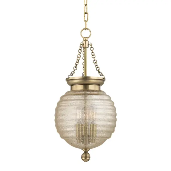 The Coolidge pendant showcases exceptional craftsmanship with its iconic beehive-shaped diffuser combining brass mesh and spun glass. The aged brass finish and spherical cast metal details create a sophisticated focal point.