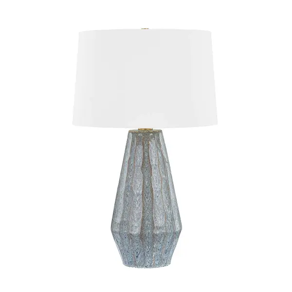 This sophisticated table lamp combines aged brass metalwork with a ceramic base in a swept coast finish, creating a refined transitional aesthetic. The single-light design offers versatile ambient lighting for residential and hospitality settings.