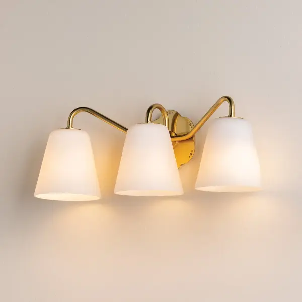 The Leonella sconce combines vintage botanical charm with modern functionality. Swooping Aged Brass arms and floral-shaped backplate with decorative perforations create visual interest, while matte white bell-shaped shades provide powerful downlight for daily routines.