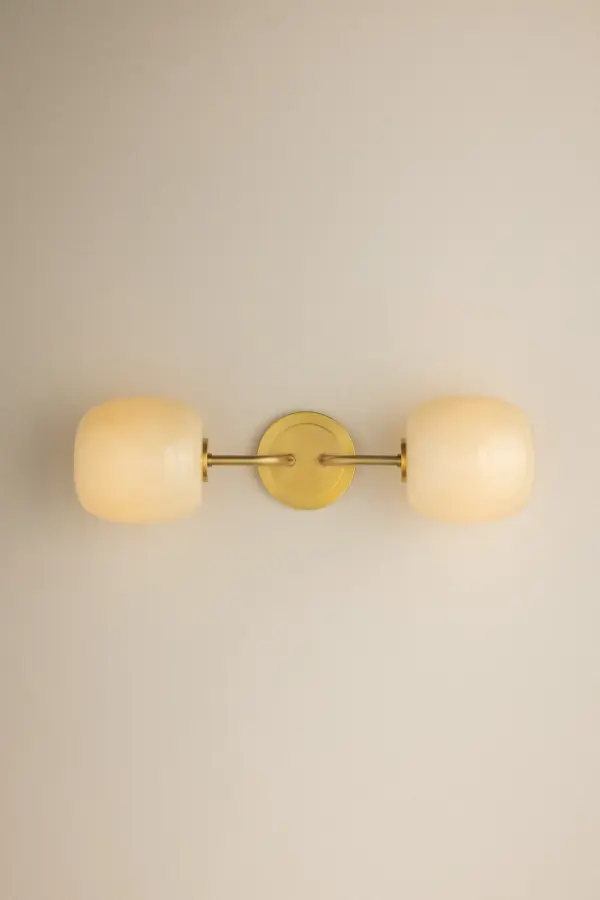 The Lisette vanity light brings sophisticated geometric design with botanical influences to bathroom spaces. Featuring shiny cream opal glass shades with delicate fluted edges and an Aged Brass finish, it delivers both functional illumination and decorative appeal. - alternate view