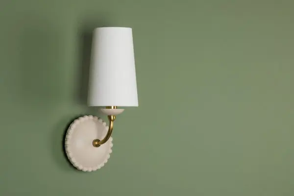 The Rhea Wall Sconce brings refreshing retro charm with its antique ivory ceramic body and scalloped sphere accents. Paired with aged brass and a white linen shade, it delivers subtle sophistication perfect for traditional and transitional spaces. - alternate view