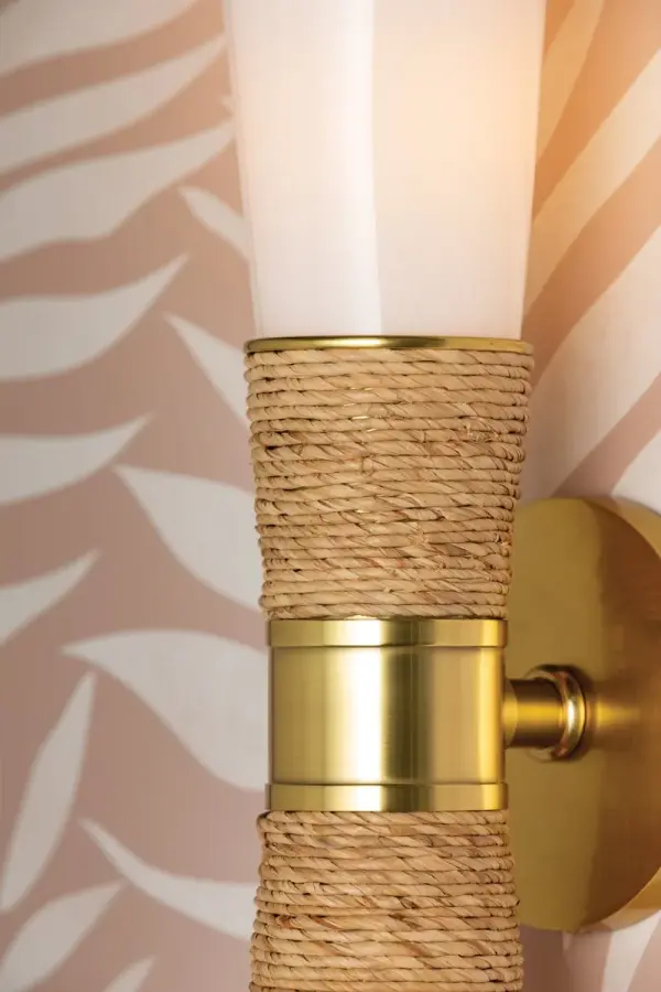 The Mica Wall Sconce beautifully blends coastal charm with quiet luxury through its wrapped raffia detail and sleek aged gold brass finish. Perfect for creating ambient lighting in powder rooms and kitchens, this designer fixture adds an approachable yet sophisticated touch to any space. - alternate view