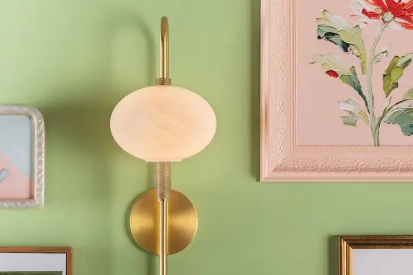 The Delphine Wall Sconce combines vintage charm with modern sophistication through its distinctive looping racetrack arm and opal glass shade. Knurled details add decorative interest to the aged brass frame. - alternate view