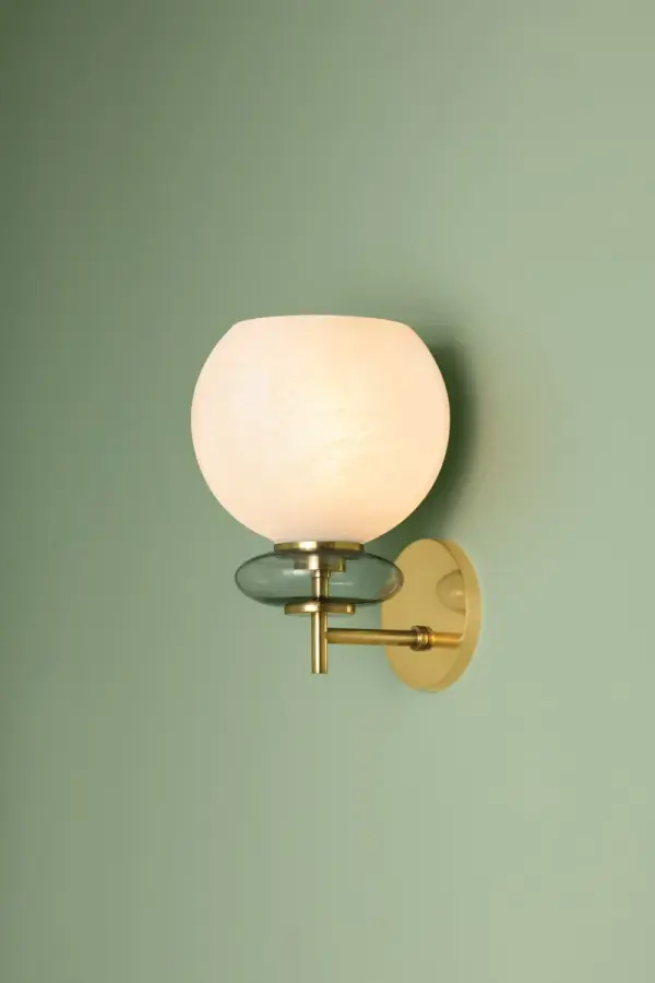 The Alexia Wall Sconce features a striking totemic design with a cloud glass orb stacked above an iridescent bubble, pierced by lustrous Aged Brass metalwork. This delicate yet charming fixture adds artistic sophistication to any space.