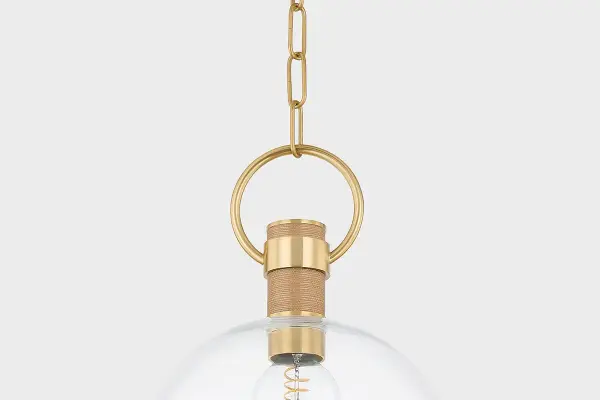 The Catrine Pendant masterfully blends industrial design with organic elements, featuring a large glass globe suspended by an oversized pin and loop in Aged Brass, softened by natural grass cloth wrapping for textural interest. - alternate view