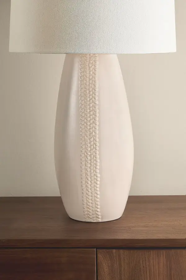 The Shavani brings sophisticated warmth to any space with its elongated ceramic base featuring unique vertical whipstitch-inspired texture. The creamy Honeydew glaze paired with aged brass hardware and generous linen shade creates an earthy yet refined aesthetic perfect for transitional interiors. - alternate view