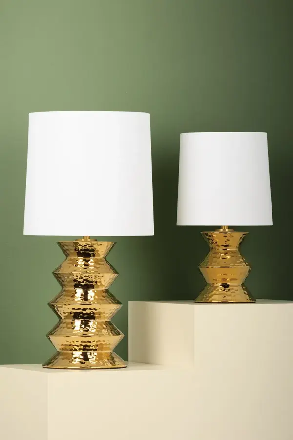 The Zoe Table Lamp brings artisanal elegance to any space with its stacked ceramic gold base featuring a distinctive dimpled texture. The white linen drum shade provides soft, diffused light while the metallic finish beautifully reflects ambient illumination. - alternate view