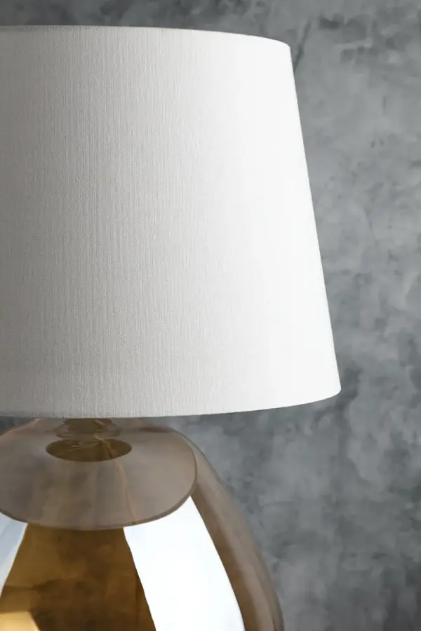 The Thea Table Lamp combines artisanal craftsmanship with contemporary elegance. Its unique luster finish and plated champagne amber glass create a warm, sophisticated ambiance, while the French-wired detail and linen drum shade add refined touches. - alternate view