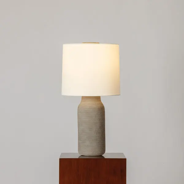 The Stassi table lamp brings warmth and texture to modern interiors with its artisanal ceramic base in grey-brown matte glaze. Horizontal etched linework and an oversized ceramic finial add sculptural interest, while the white linen drum shade provides soft, balanced illumination. - alternate view