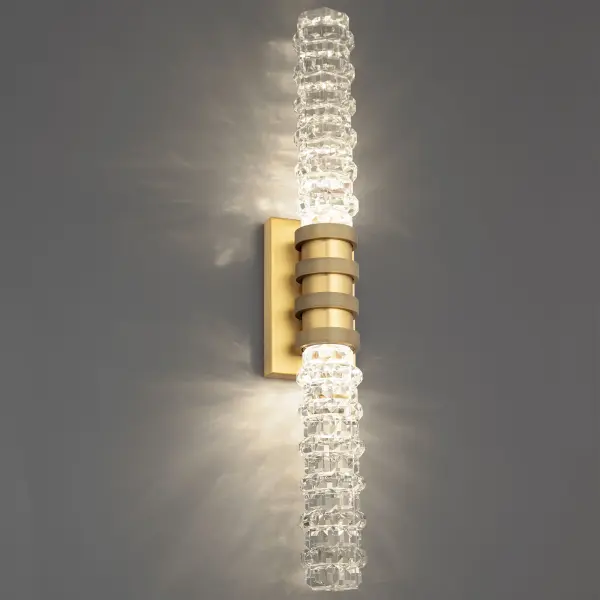 In a striking combination of materials, this bath vanity light showcases sleekly layered crystal rings on a tiered metal base offering a harmonious balance of modern design and timeless elegance. Anchored by a gleaming backplate, the design elegantly refracts light for a dazzling effect.