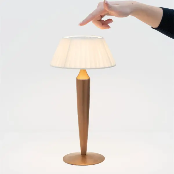The Flaminia combines classic elegance with modern cordless convenience. Its pleated fabric shade and matte gold finish create a refined aesthetic, while touch controls offer adjustable brightness and three color temperatures. Perfect for creating ambiance without cords. - alternate view