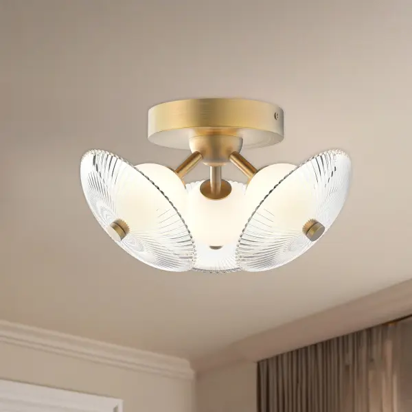 The Hera flush mount combines feminine elegance with practical functionality. Its brushed gold frame and clear ribbed glass shade create sophisticated visual interest while the integrated 3000K LED provides warm, inviting illumination. - alternate view