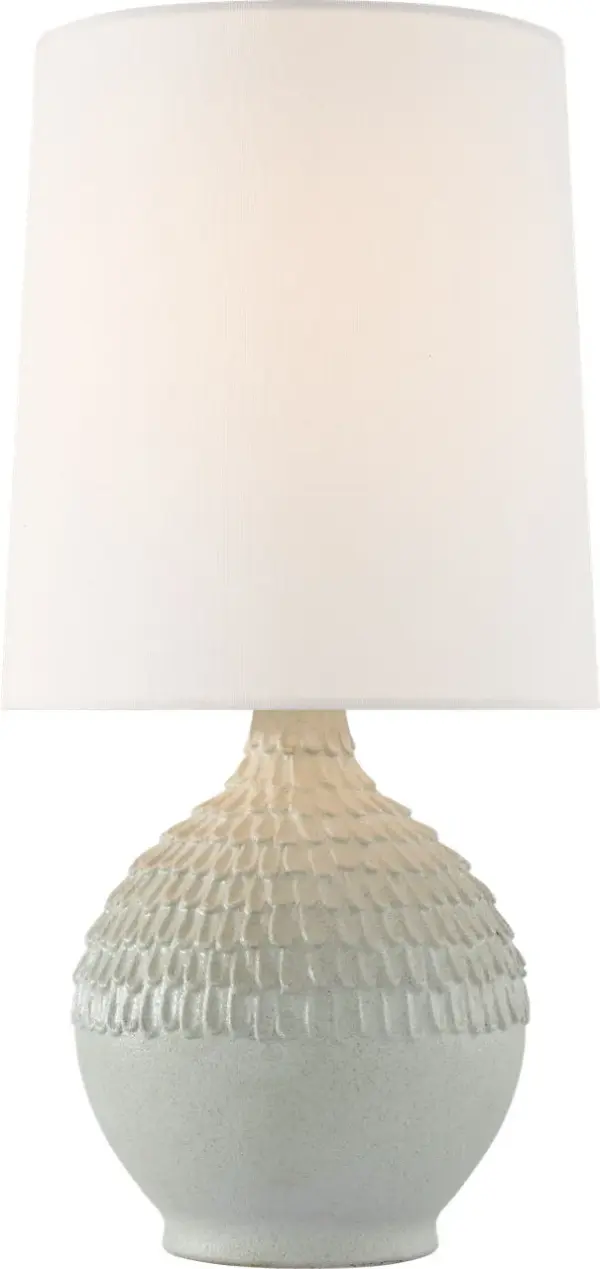 The Morava table lamp showcases hand-carved volcanic white ceramic with organic texture that brings artisanal character to any space. Its compact 17" height and neutral linen shade make it versatile for bedrooms, living areas, and offices.