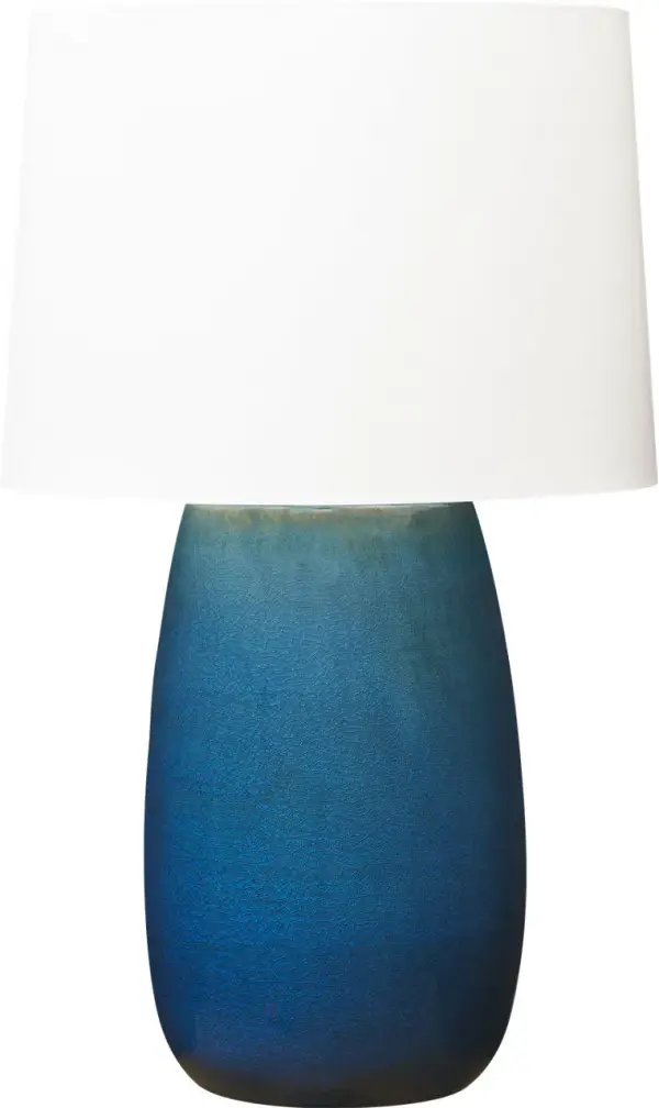 The Roma Table Lamp by Barbara Barry combines refined design with artisanal craftsmanship. Its elongated oval ceramic base features a distinctive deep ocean crackle finish, while the tailored linen shade provides warm, diffused illumination perfect for both modern and traditional spaces.