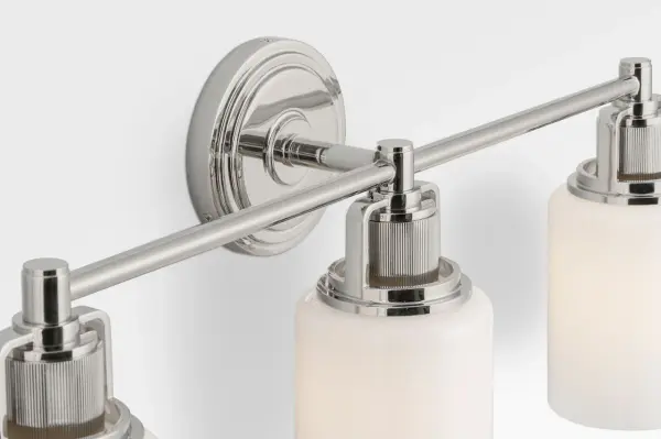 The Ashford 24" vanity light combines industrial precision with refined simplicity, featuring dual white cylindrical glass shades and vertically knurled socket covers that echo popular bath fittings. - alternate view