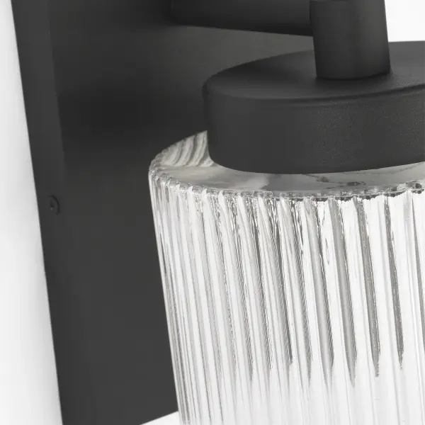 The Ronde Medium Outdoor Wall Lantern combines vertical ribbed glass with a sleek metal frame in Textured Black. Wet-rated for durability and available with LED efficiency, it suits patios, porches, and entryways with transitional to contemporary appeal. - alternate view