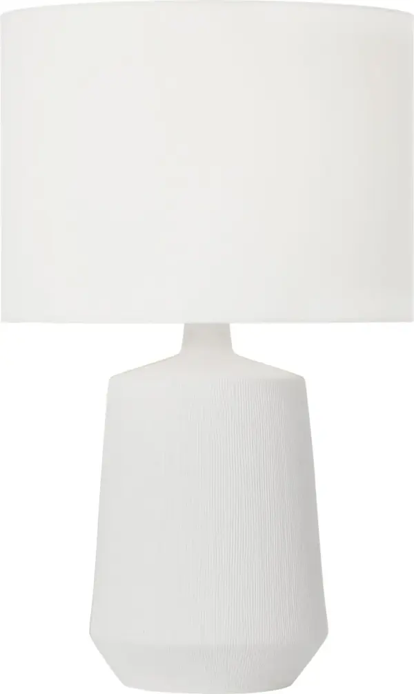 The Panola Medium Table Lamp combines handcrafted artistry with contemporary design. Its matte white ceramic base features vertical etchings that create visual texture, while brass detailing adds warmth. The white linen drum shade provides soft, diffused lighting perfect for ambient illumination. - alternate view